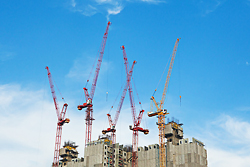 Photo of a skyscraper being constructed by cranes against a blue sky background.