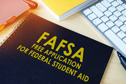 Desk with a keyboard visible along with a spiraled notebook with the following words on the cover; "FAFSA, free application for federal student aid".