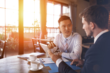 Two males in business attire converse over a coffee. 