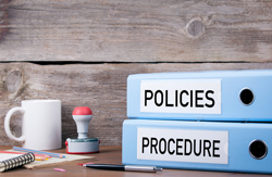 Two baby blue binders, one that says "policies" and the other that says "procedures", sit next to assorted office supplies.