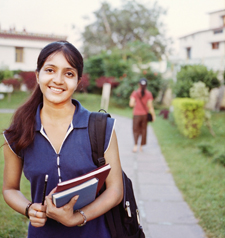 Photo of a female students holding books and wearing a backpack while walking along a concrete path.