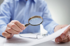 Person holding a magnifying glass up to a sheet of paper.