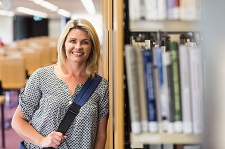 Female student smiling as she leans against a bookcase in a library.