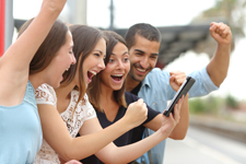 Four young adults cheering as they look at a tablet together.