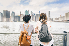 Two side-by-side people leaning against a railing by the water while looking at a cityscape.