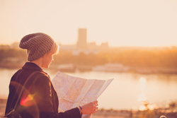 Young adult looking at a map as they appear to stand on the edge of a city.