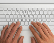 Hands resting on a keyboard that's blank except for the following text: "share your thoughts."