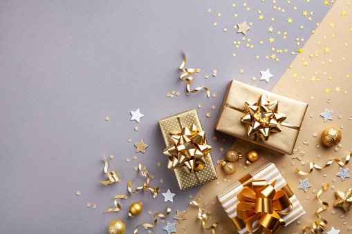 three shiny golden gifts with golden bows against a silver and gold sparkling background with gold ornaments, ribbons, and silver stars sprinkled around
