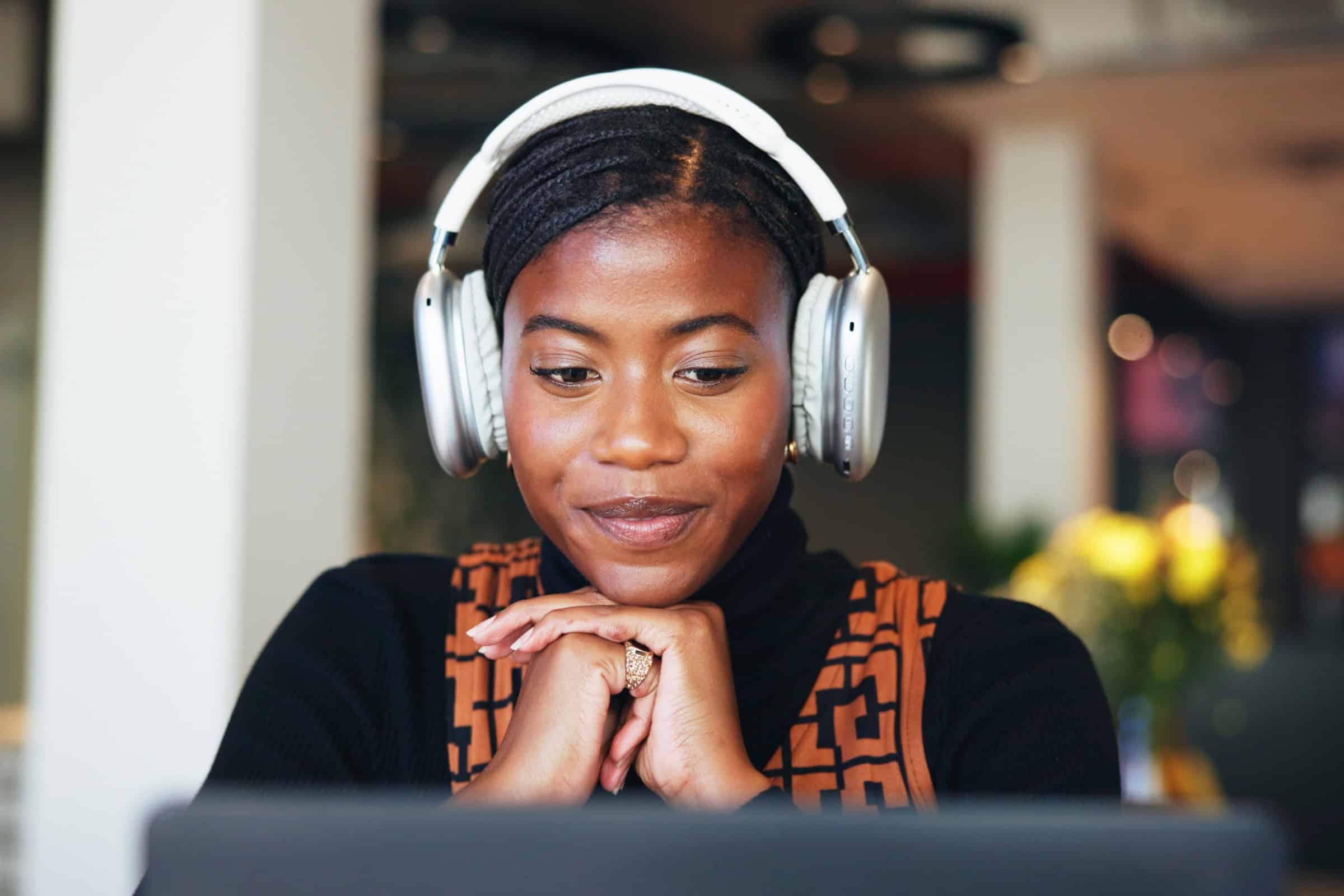 Woman wearing over-ear headphones, looking down and smiling while seated indoors