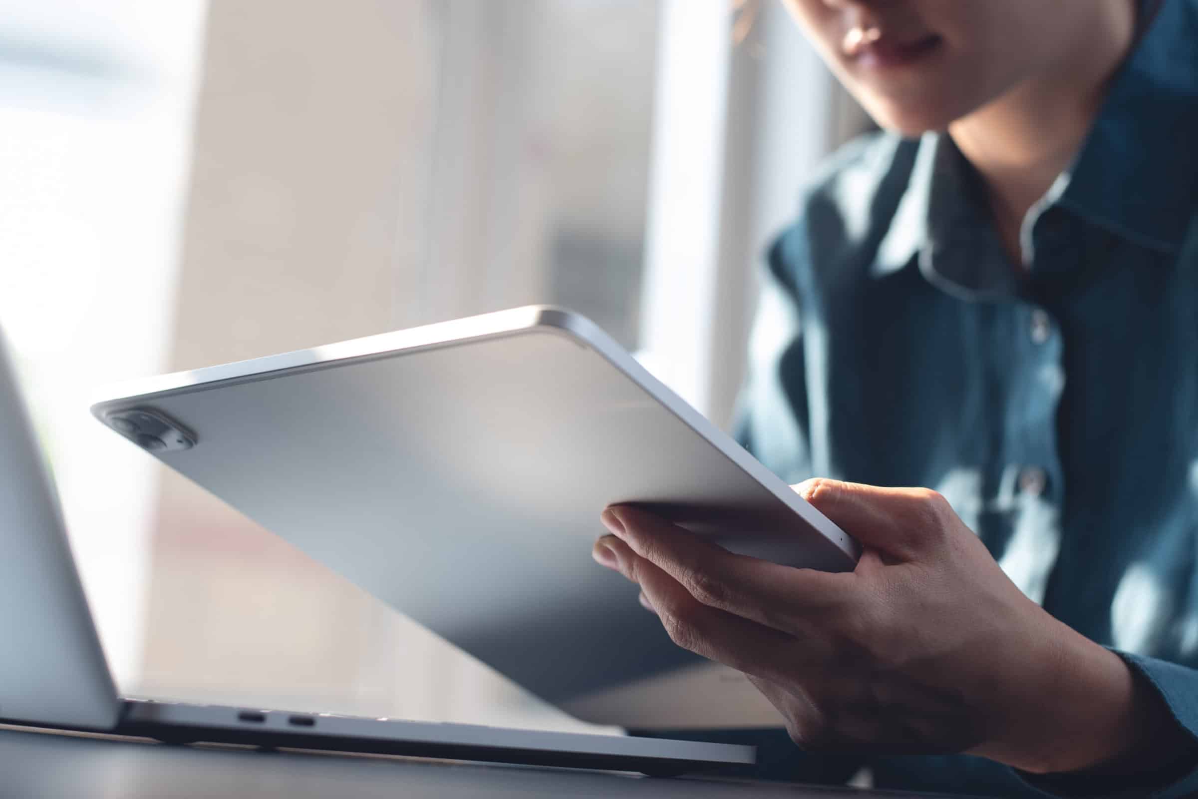 Person holding a tablet while working at a desk with a laptop nearby
