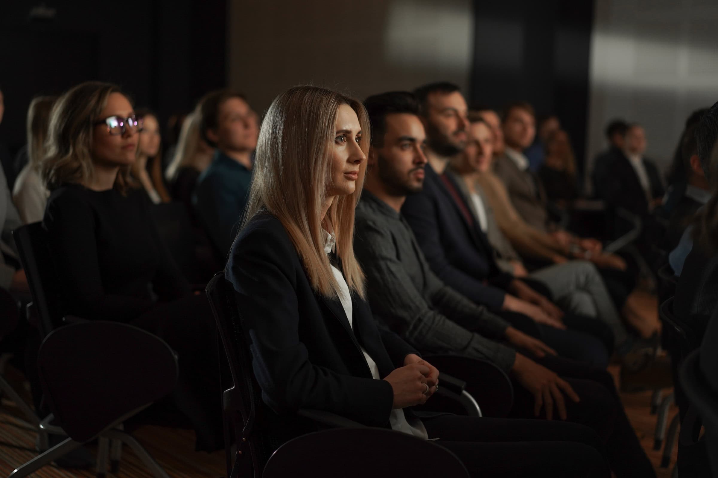 Audience members seated in a conference room, listening attentively during a presentation