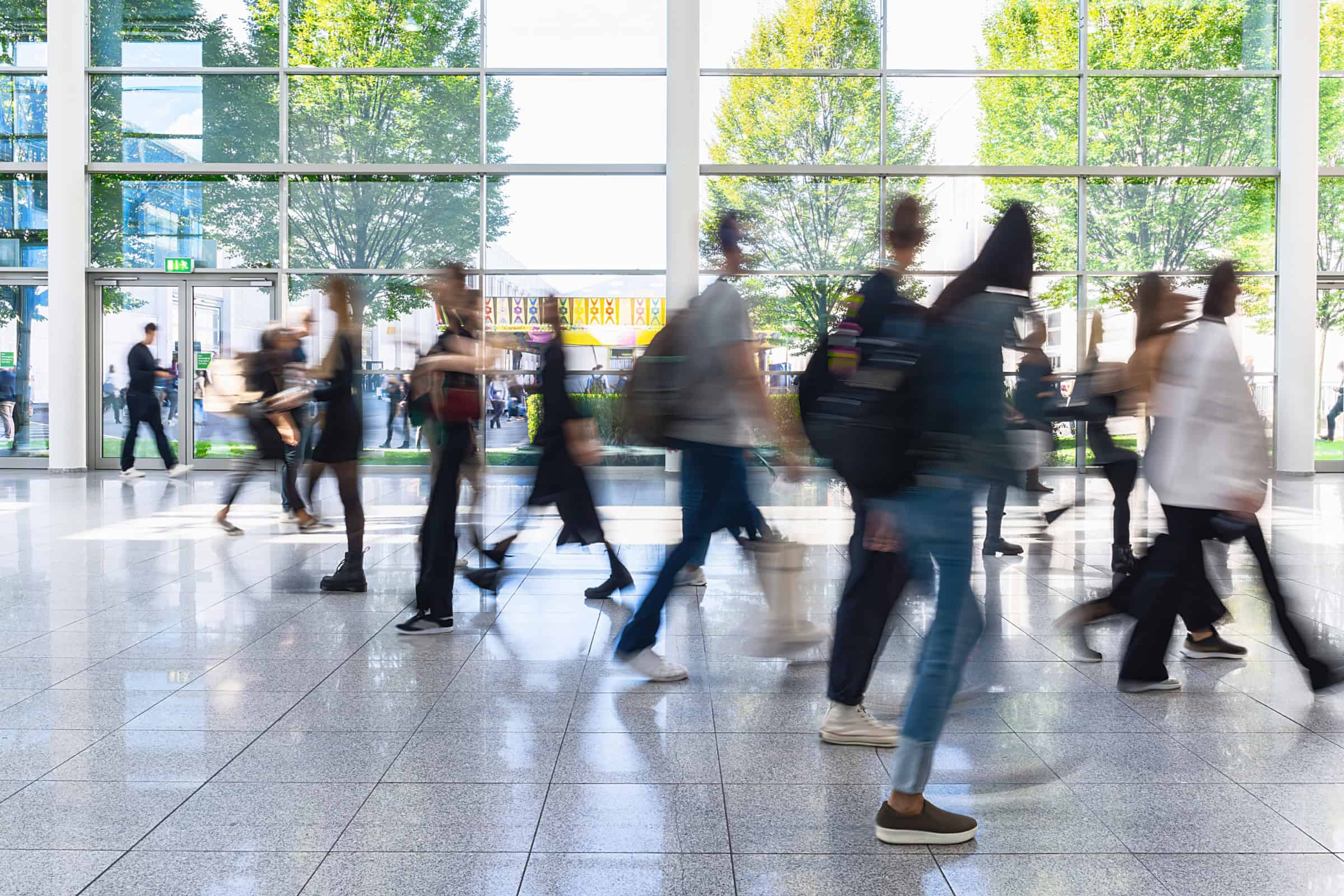 People walking through a bright office lobby, creating motion blur