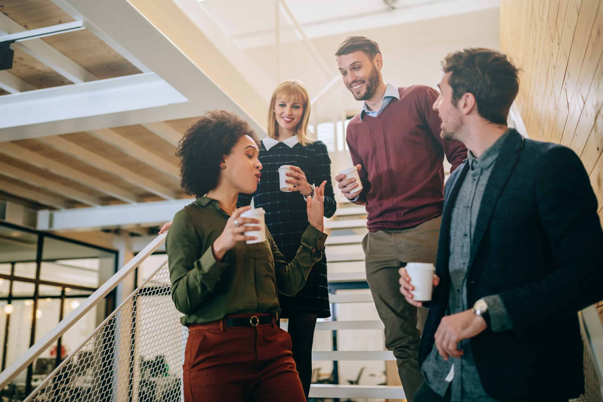 Group of coworkers chatting and holding coffee cups in a modern office stairwell