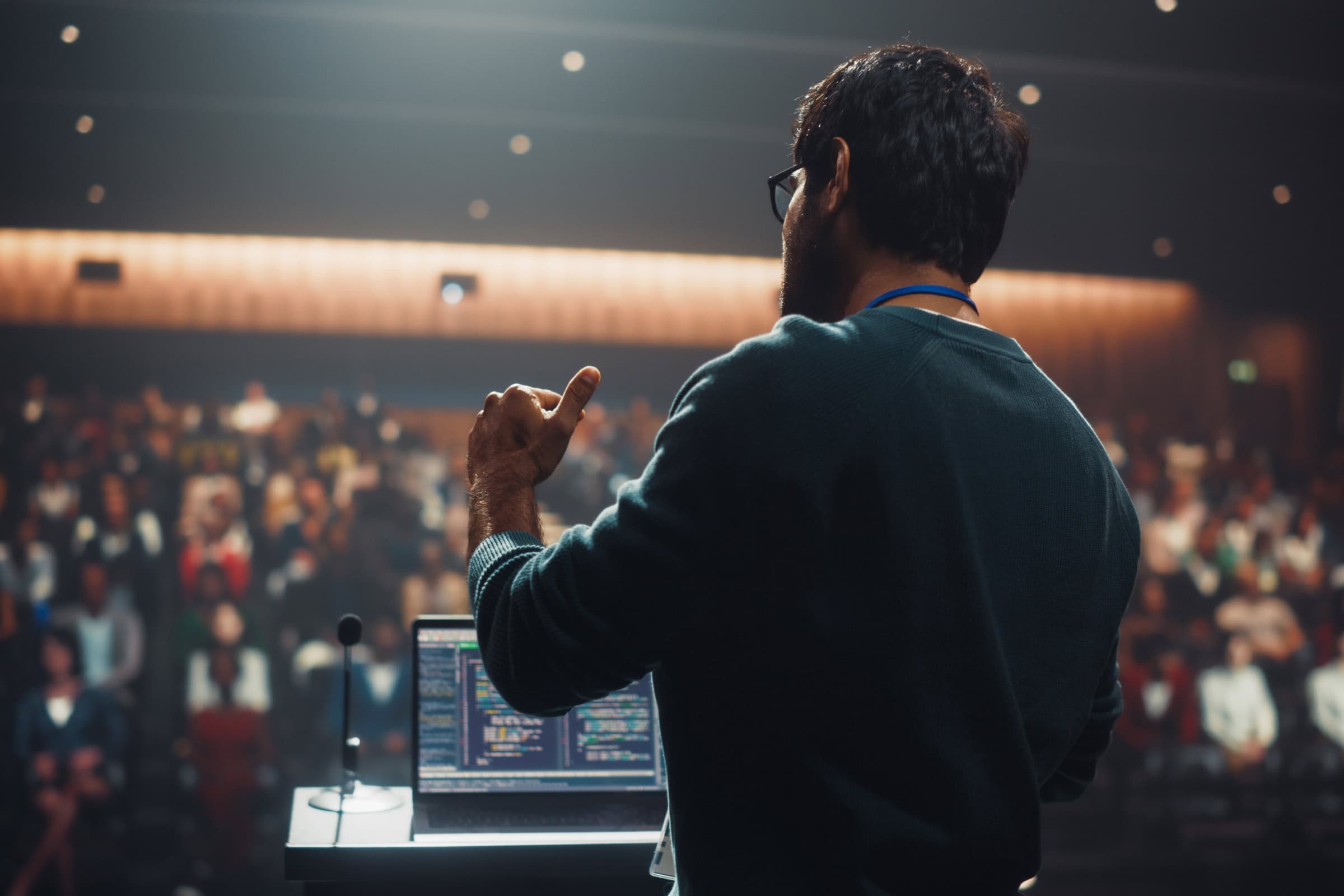 Man on stage facing a cheering crowd, gesturing with his hand during a live event