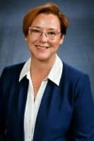 Portrait of a smiling woman in glasses wearing a navy blazer and white shirt