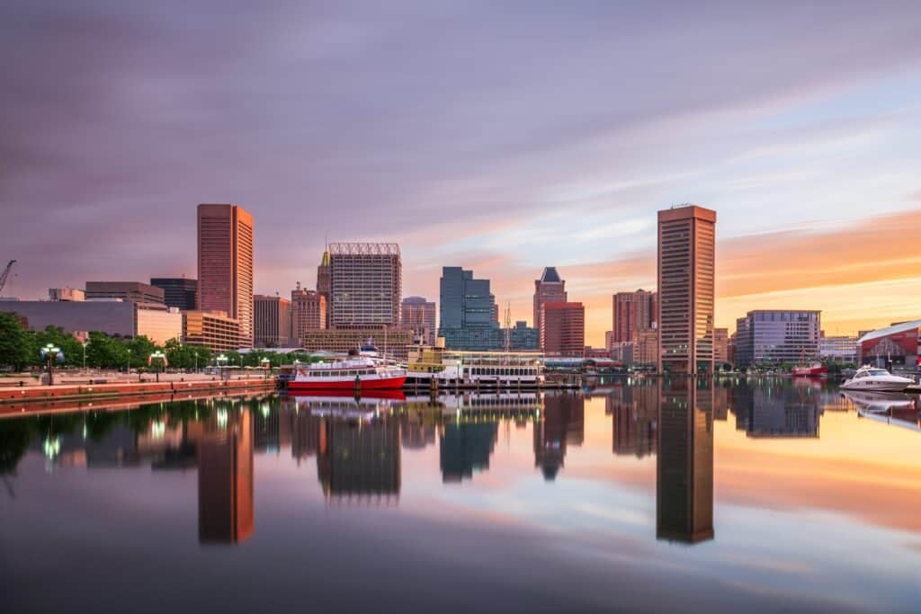 Baltimore skyline at sunset reflected in calm harbor water with boats docked in the foreground