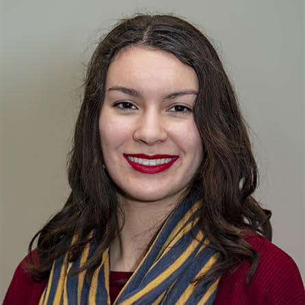 Portrait of a smiling woman with dark hair, wearing a red top and striped scarf