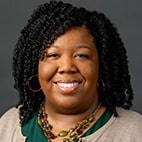 Portrait of a smiling woman with curly black hair against a gray background