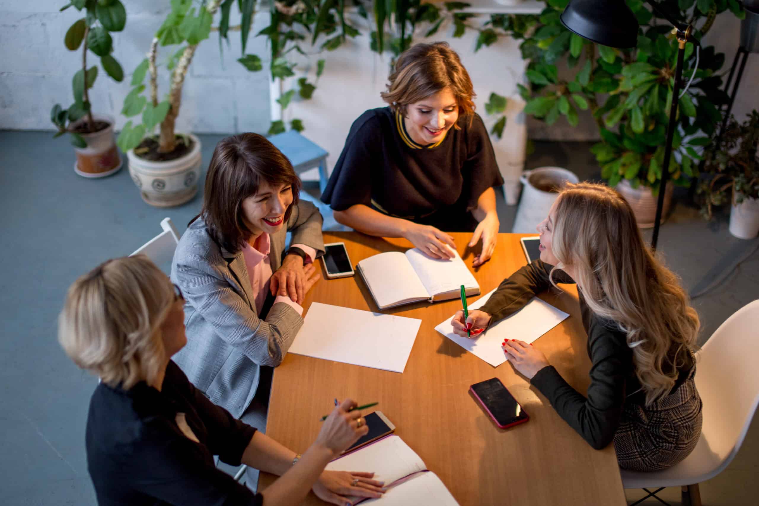 Four women in a meeting around a table, talking and taking notes