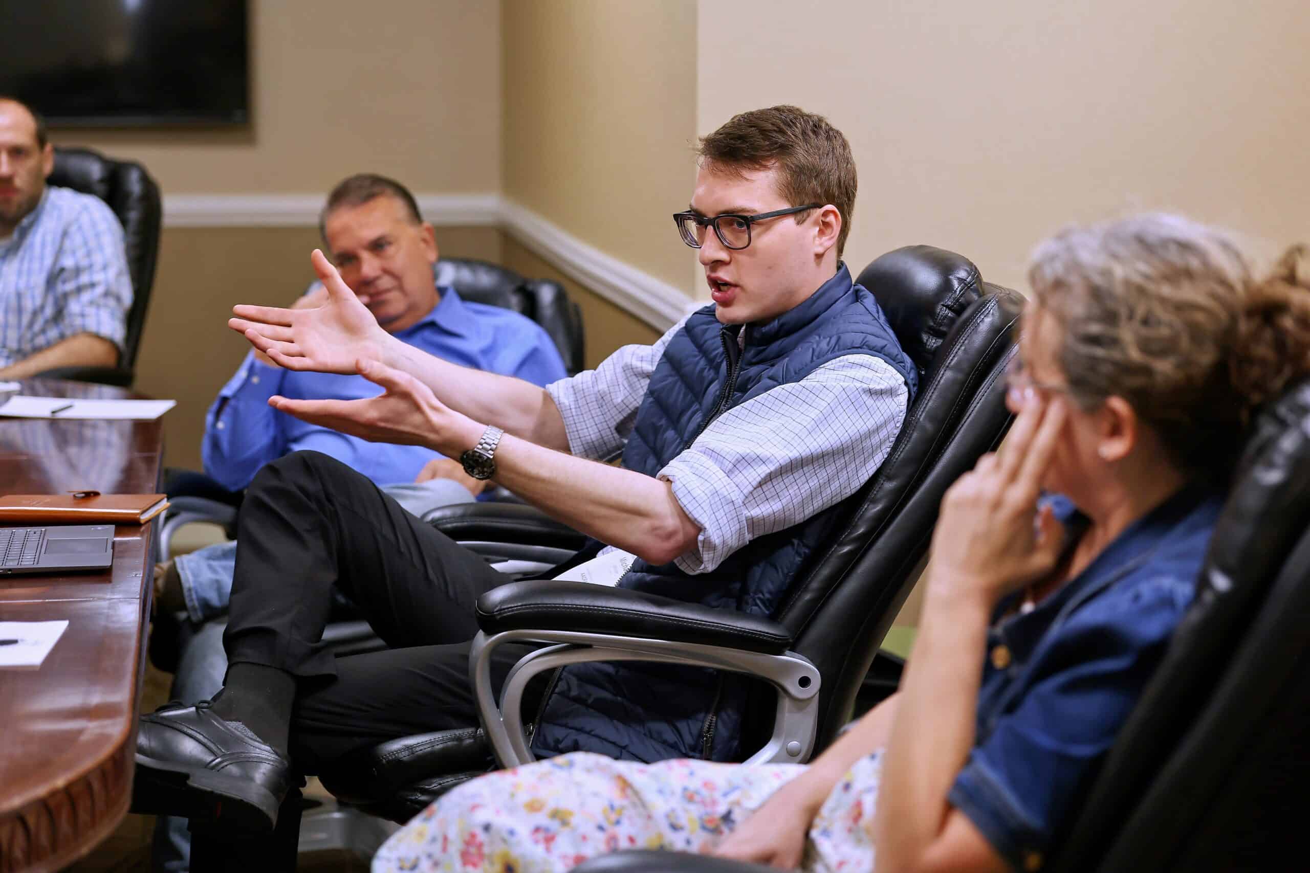 A man speaks to people at a meeting room with his hands gesturing intention