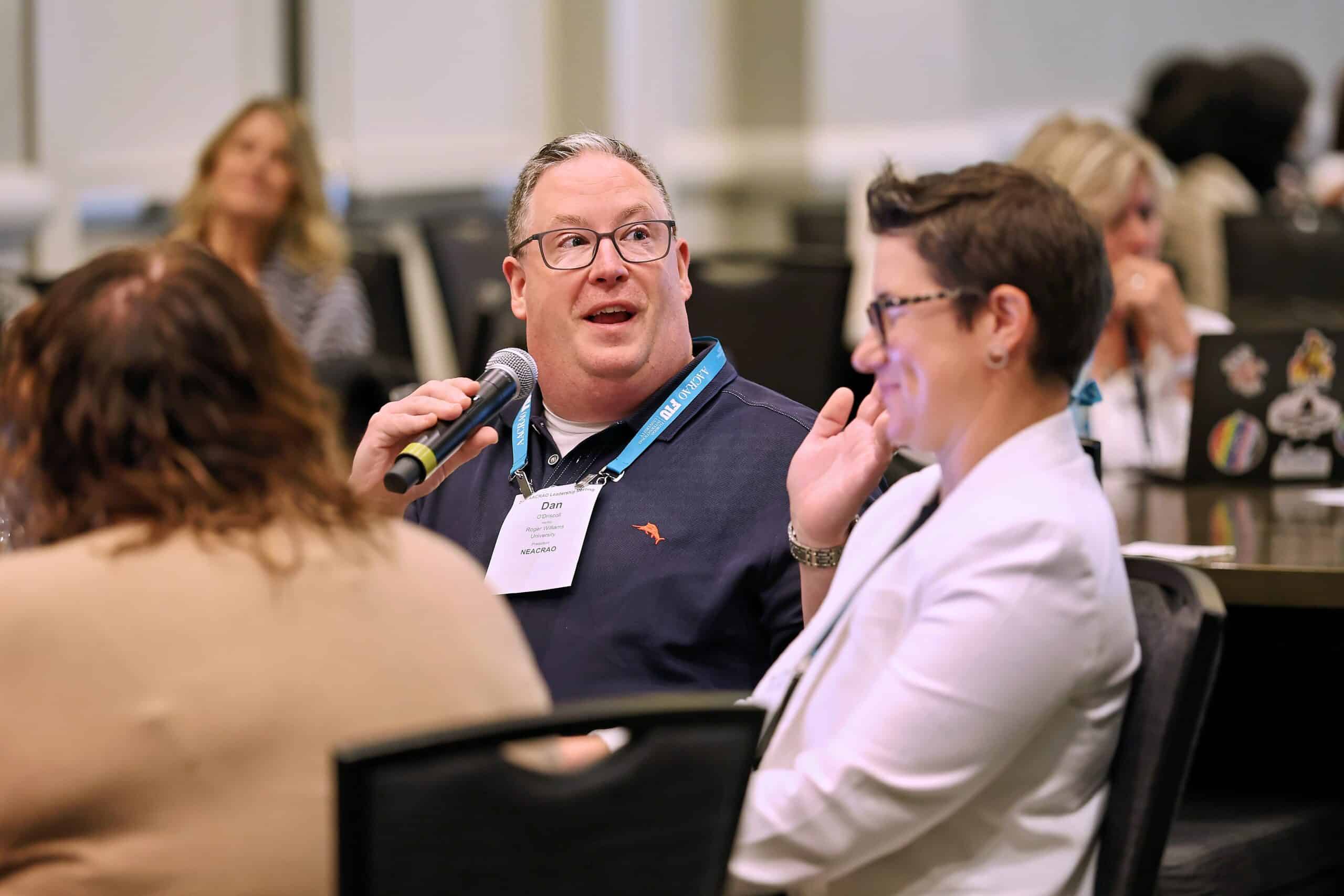 man at a table at an AACRAO event speaks to attendees