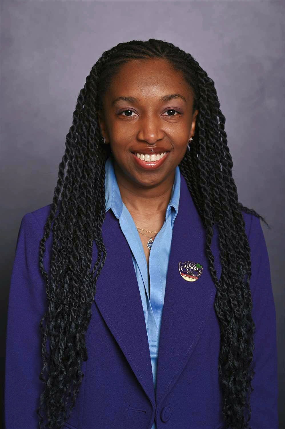 A smiling woman with long braids wearing a purple jacket