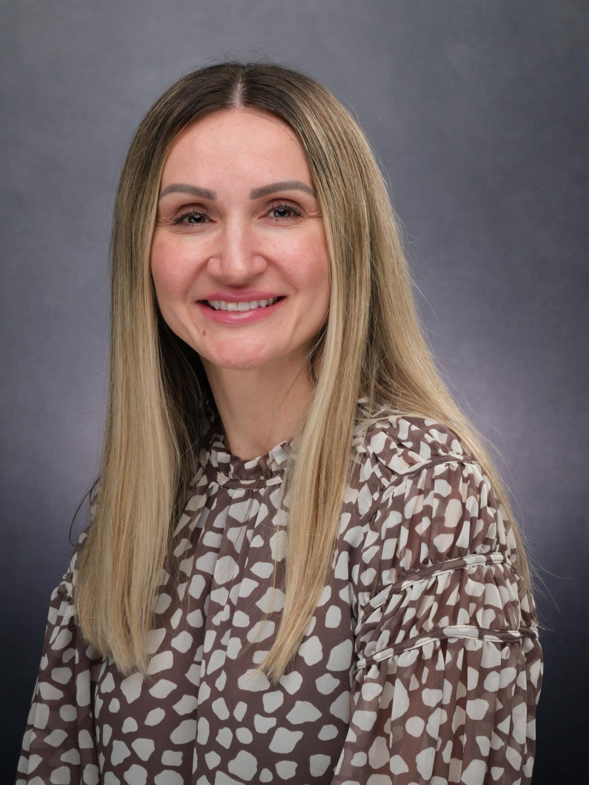 Portrait of a smiling woman with long blonde hair against a gray background