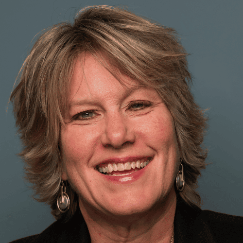 Smiling woman with short gray hair and earrings against a blue-gray background