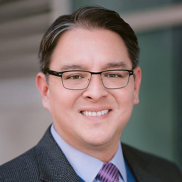 Portrait of a smiling man wearing glasses, a suit, and a tie