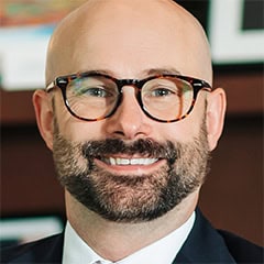 Portrait of a smiling bald man with glasses and a beard in a suit