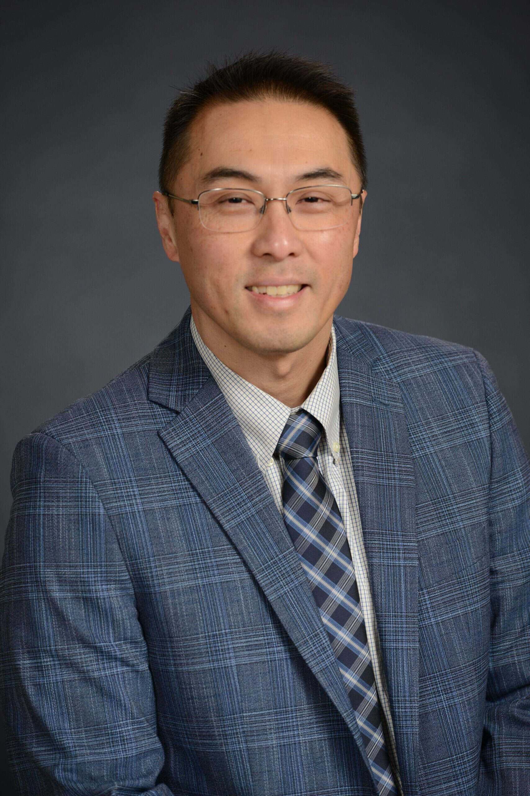 Portrait of a man wearing glasses, a blue plaid suit, and a striped tie