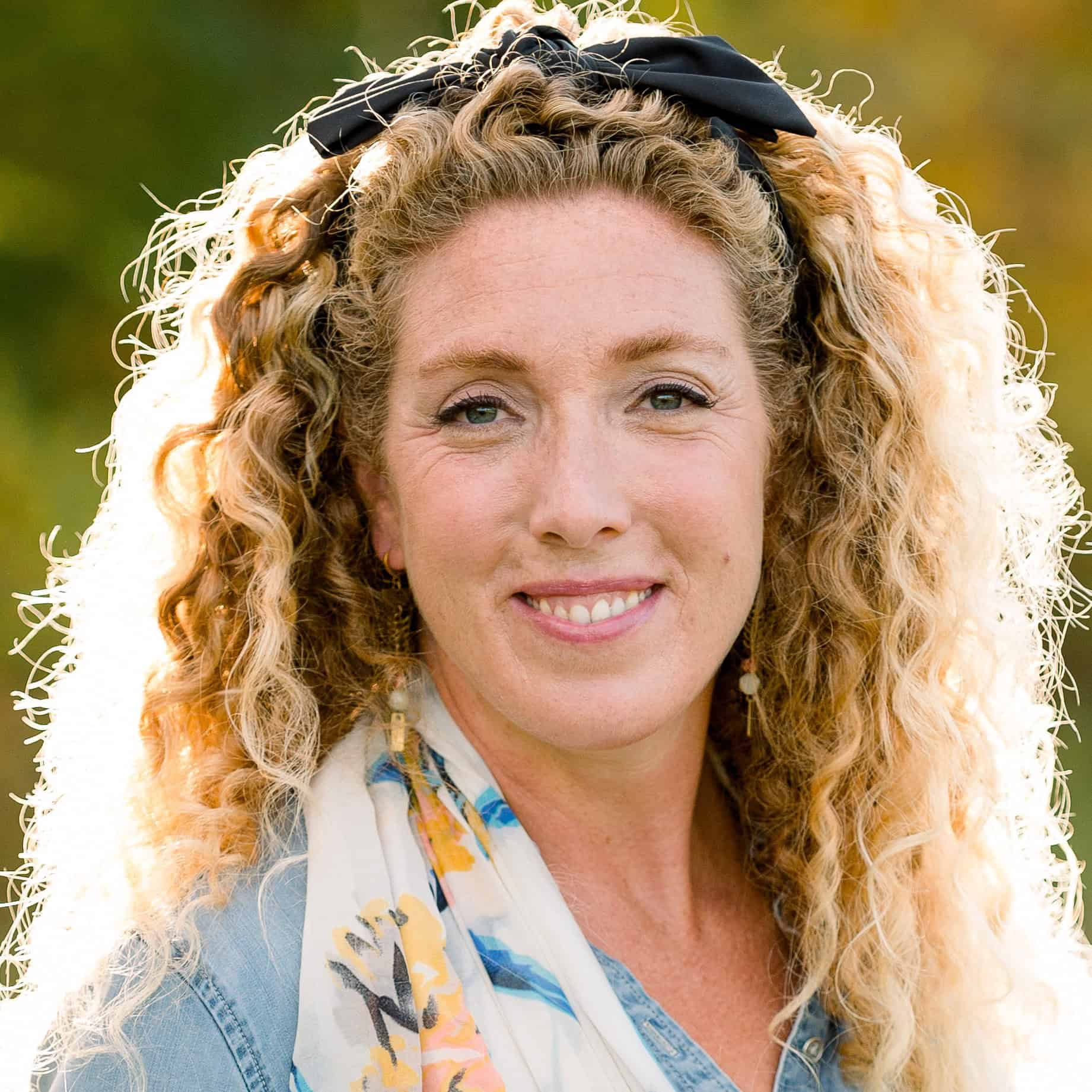 Portrait of a smiling woman with curly blonde hair and a black headband outdoors