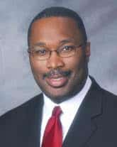 Portrait of a man in a suit, white shirt, and red tie wearing glasses