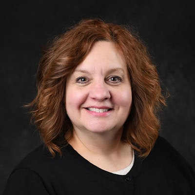 Portrait of a smiling woman with shoulder-length auburn hair against a dark background