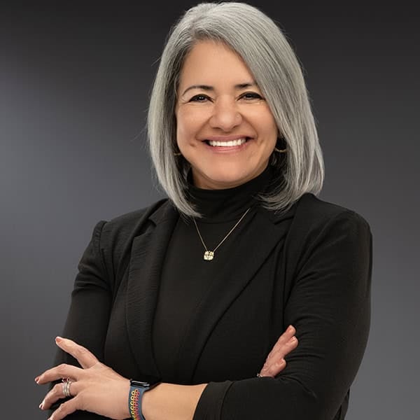 Portrait of a smiling woman with gray hair in a black outfit against a gray background
