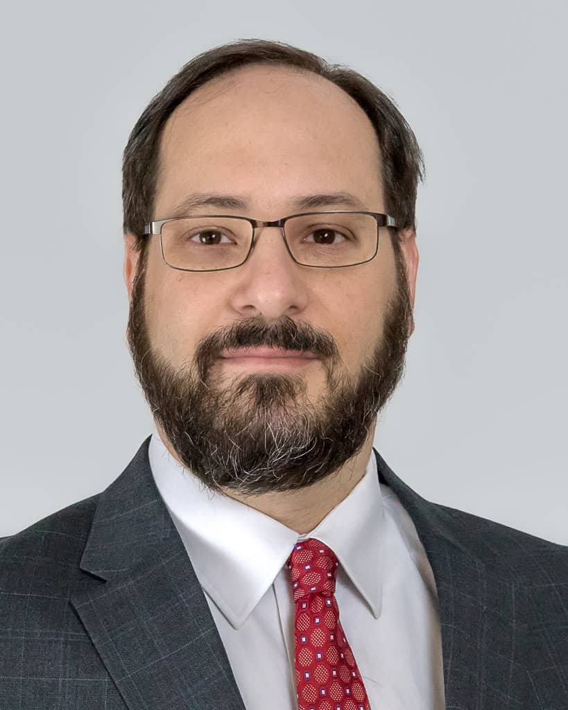 Portrait of a man wearing glasses, a suit, and a red tie