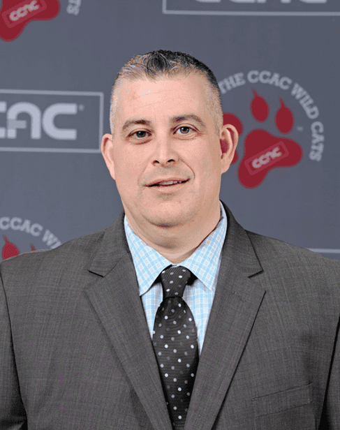 Portrait of a man in a suit and tie in front of a CCAC Wild Cats backdrop