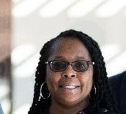 Portrait of a woman wearing glasses and hoop earrings, smiling at the camera