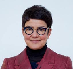 Portrait of a woman with short dark hair and round glasses, wearing a burgundy jacket and black turtleneck