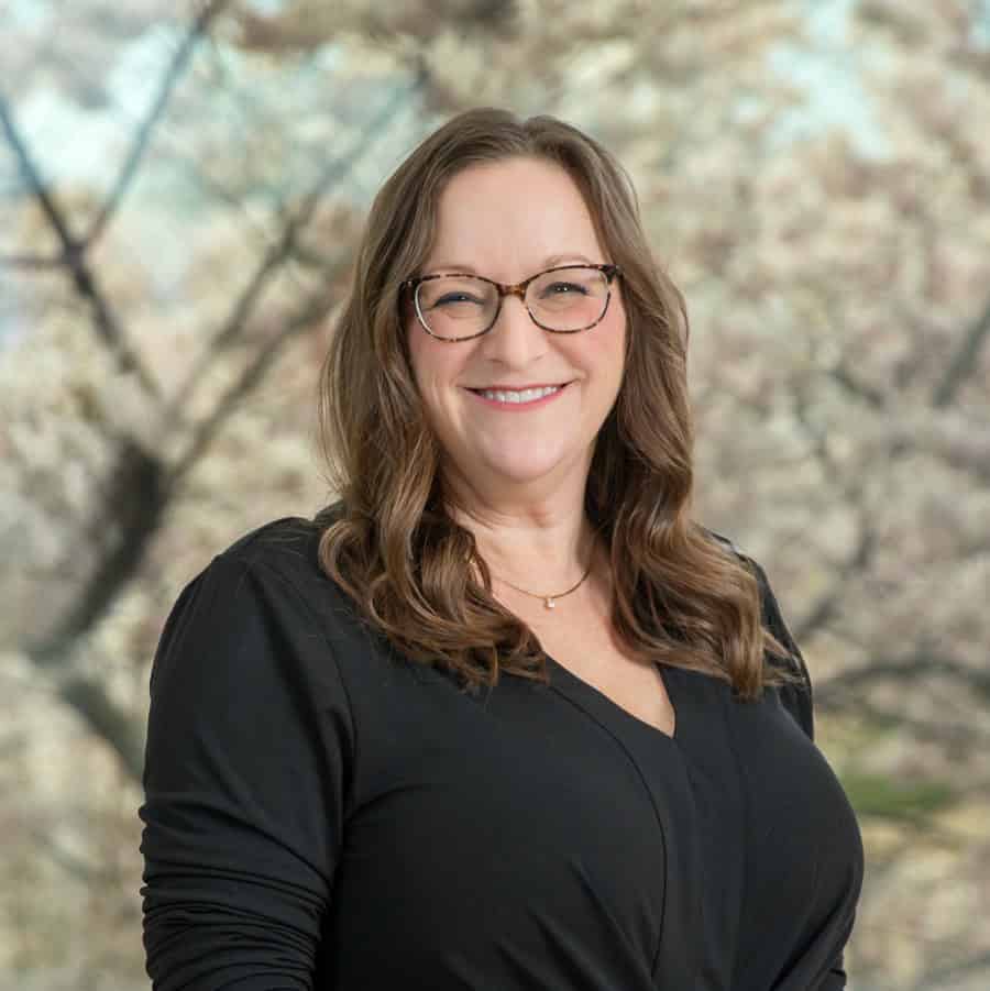 Portrait of a smiling woman wearing glasses and a black top outdoors