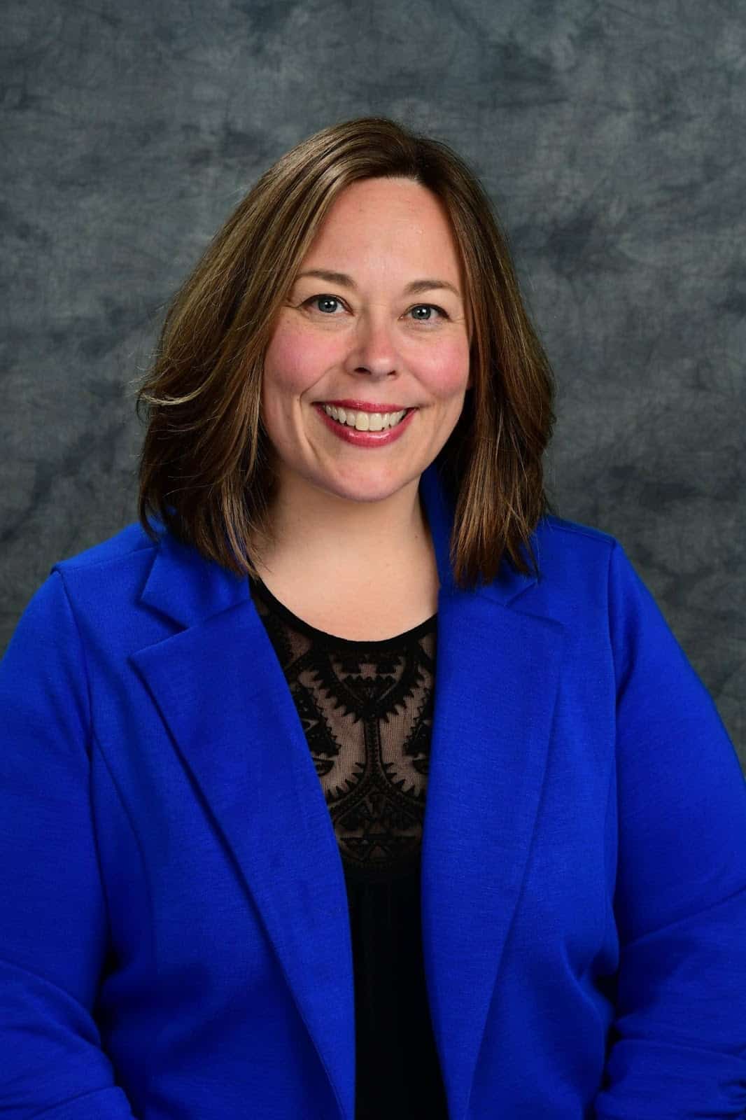 Portrait of a smiling woman in a blue blazer against a gray studio backdrop