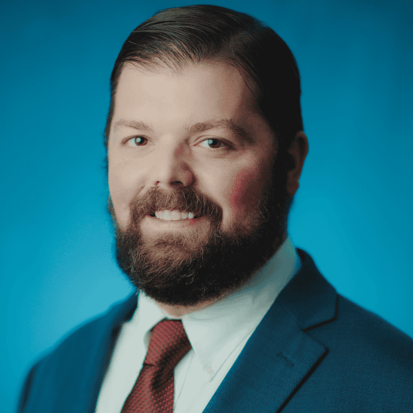 Portrait of a bearded man in a suit and red tie against a blue background