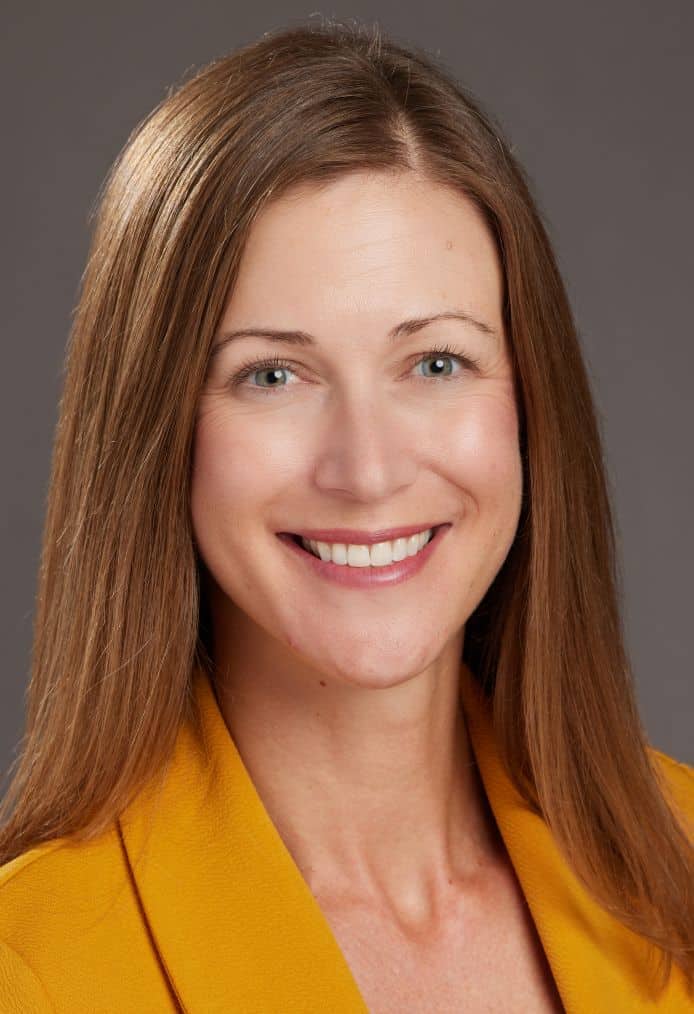 Portrait of a smiling woman with long brown hair wearing a yellow jacket