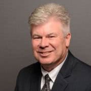 Portrait of a smiling man in a suit and tie against a gray background