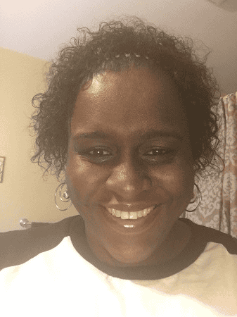 Smiling woman with curly hair and hoop earrings, wearing a white shirt with black sleeves