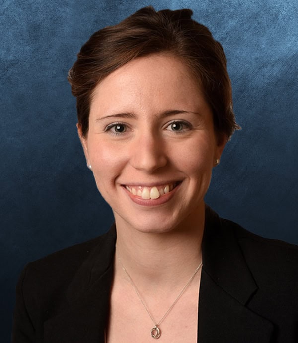 Portrait of a smiling woman in a black blazer against a blue background