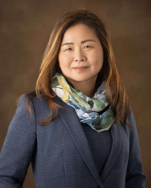 Portrait of a woman wearing a blue blazer and patterned scarf against a brown background