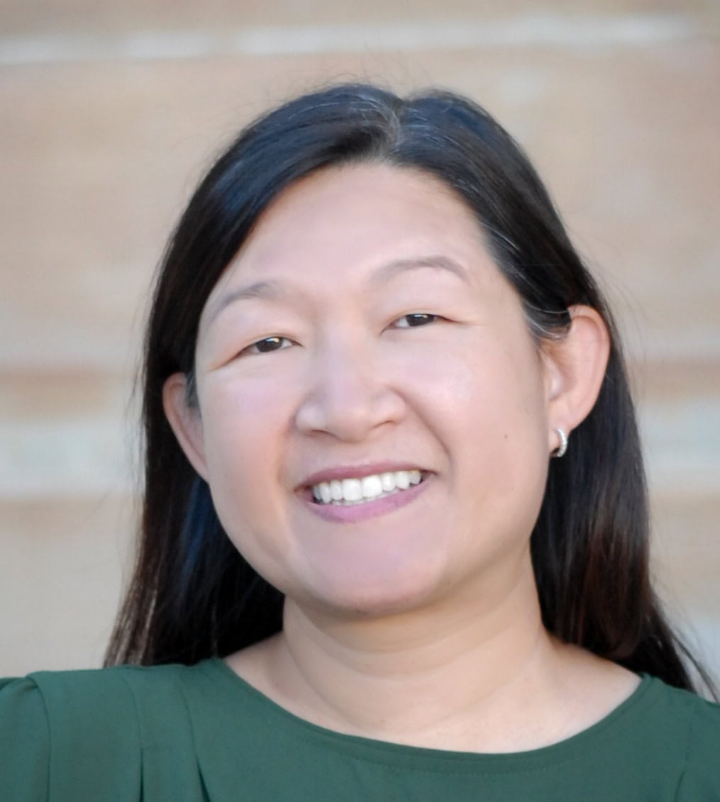 Portrait of a smiling woman with long dark hair wearing a green top