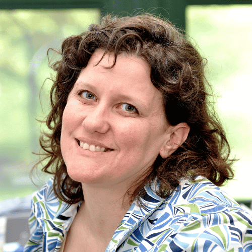 Portrait of a smiling woman with curly brown hair wearing a patterned shirt
