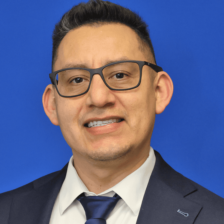 Portrait of a man in glasses wearing a suit and tie against a blue background